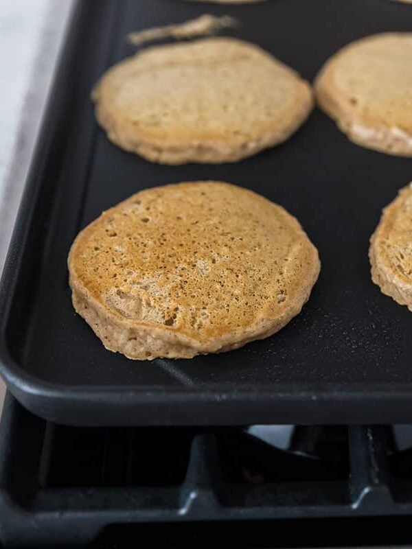 Golden brown apple pancakes cooking on a stovetop griddle after being flipped.