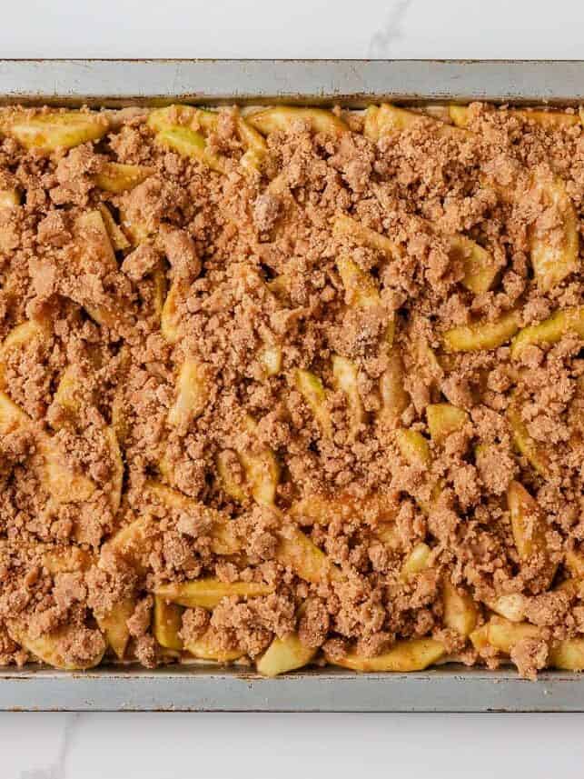 Baked apple slab pie in a pan with cinnamon crumb topping sprinkled over the apple filling.