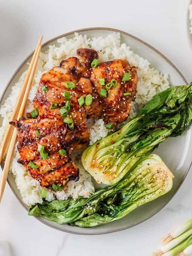 Grilled Asian chicken thighs and bok choy served over fluffy white rice with green onions and sesame seeds.