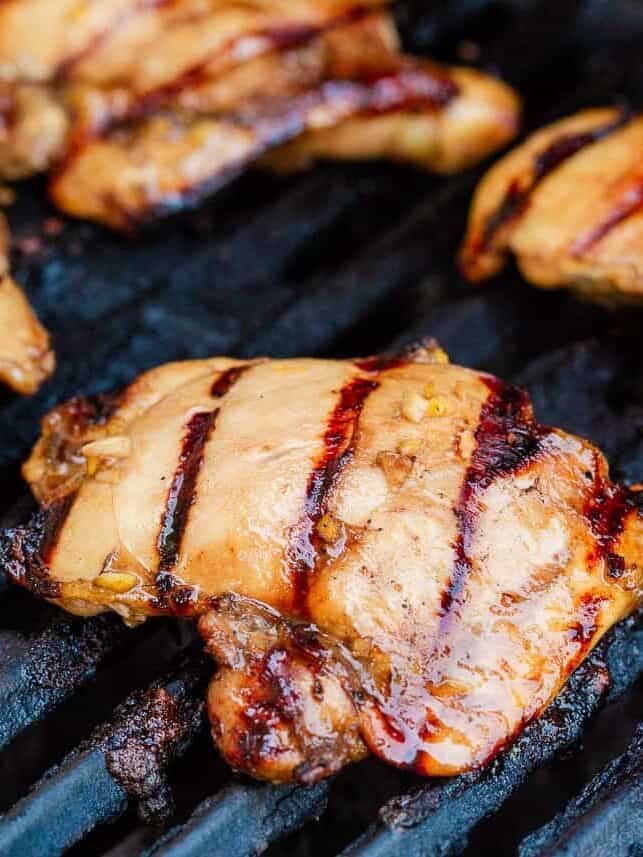 Marinated Asian chicken thighs cooking on a hot grill with charred grill marks.