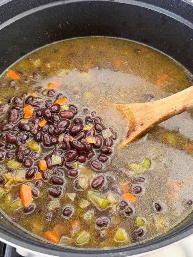 Black beans, broth and sautéed vegetables simmering in a large pot for black bean soup.