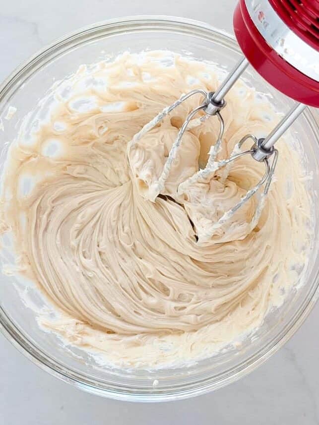 Cream cheese mixture being blended with an electric hand mixer for caramel apple cheesecake dip.