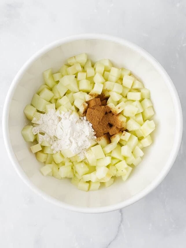 Diced apples in a bowl with spices and flour.