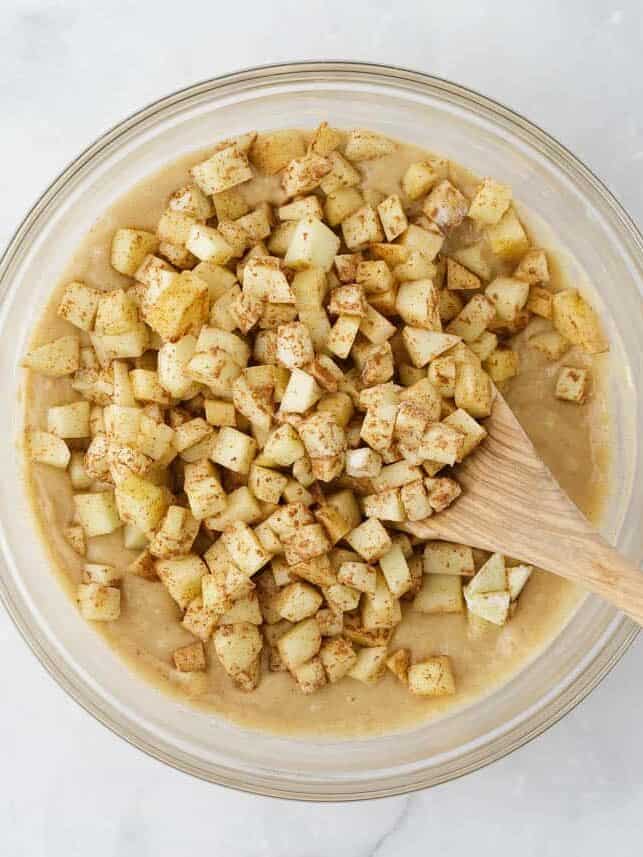 Diced apples being mixed into a muffin batter in a bowl.