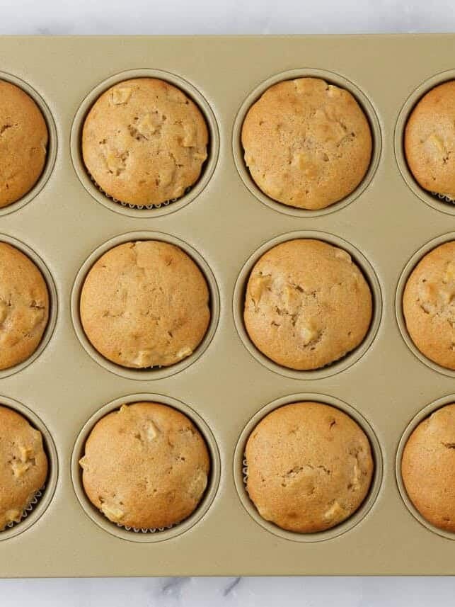 Baked cinnamon apple muffins cooling in a 12-cup muffin pan.