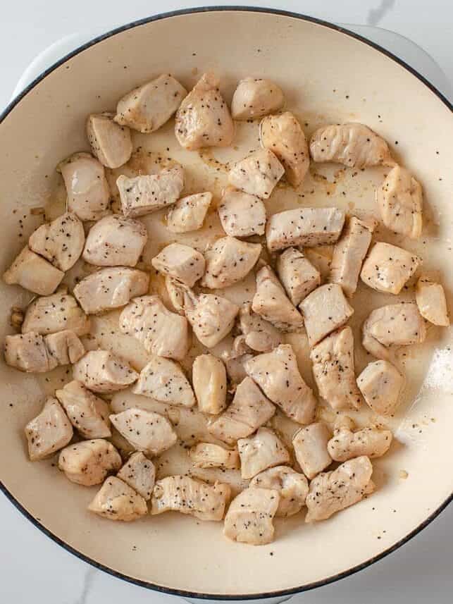 Bite-sized chicken breast pieces lightly browned in a Dutch oven.