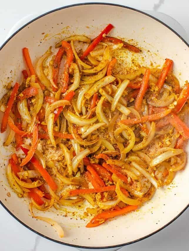 Sliced onions and red bell peppers sautéing with garlic, ginger, curry powder and cumin in a Dutch oven.