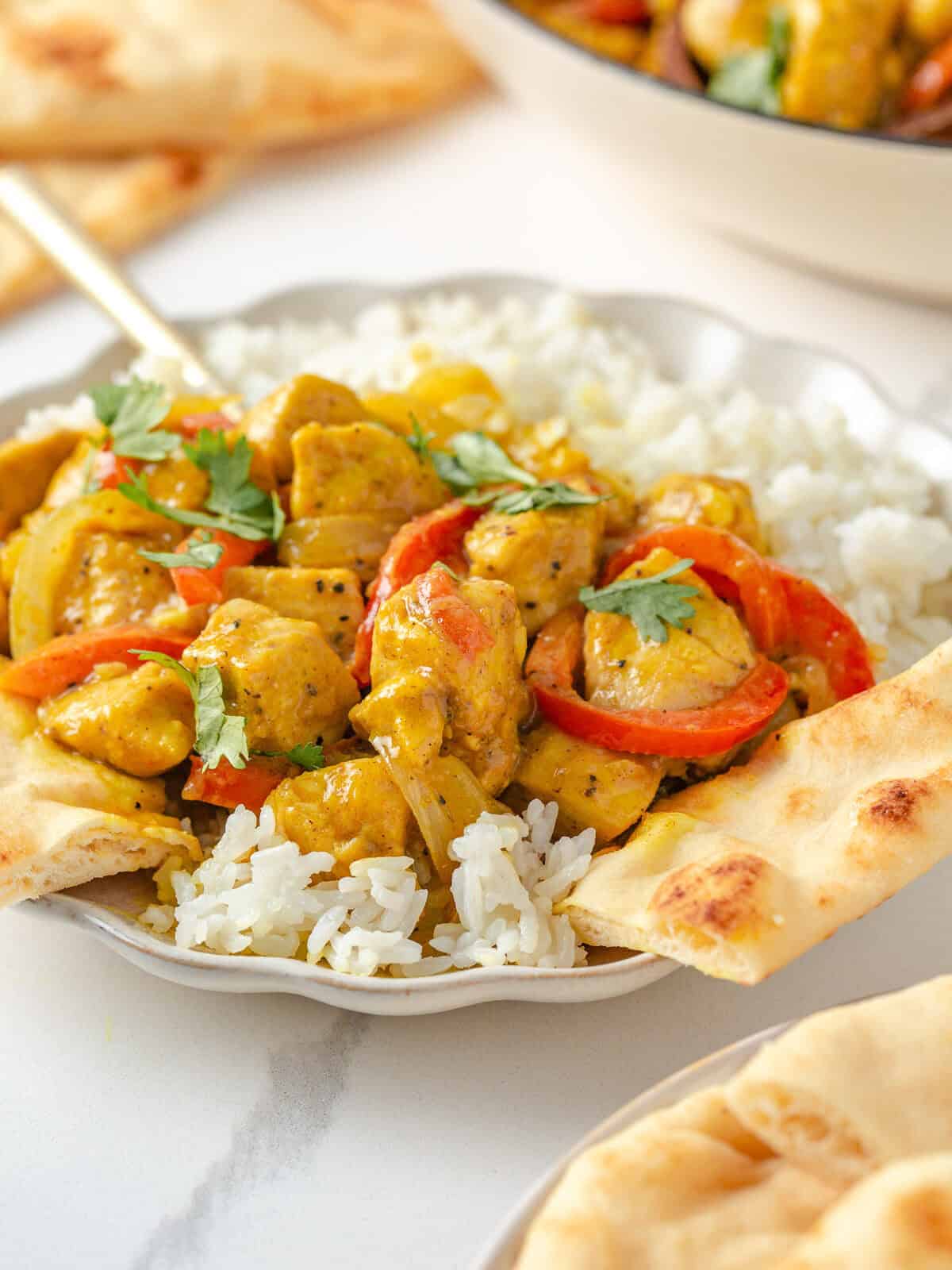 Curry coconut chicken served over rice in a shallow dish with naan on the side.
