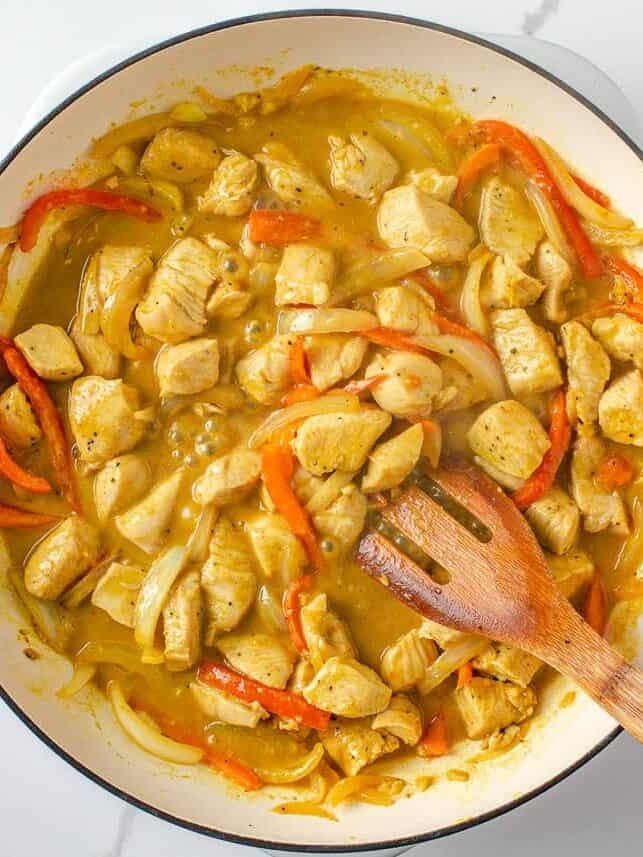 Cooked chicken, onions and red bell peppers simmering in coconut curry sauce.