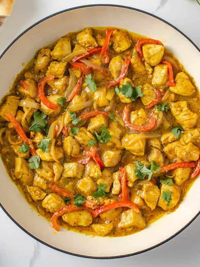 Coconut curry chicken with red bell peppers, onions and cilantro in a Dutch oven with naan on the side.