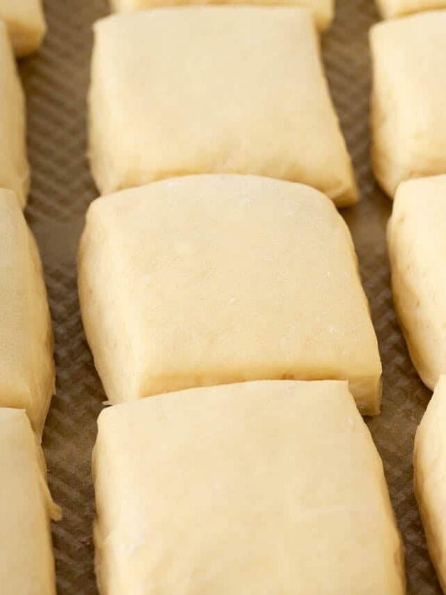 Unbaked square rolls arranged on a baking sheet after rising.
