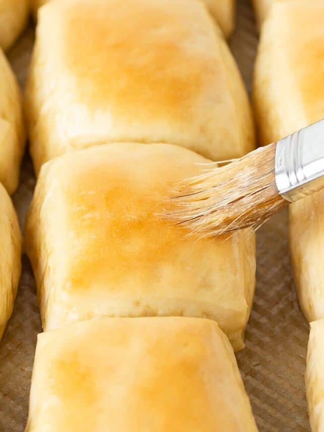Freshly baked Texas Roadhouse rolls being brushed with melted butter.
