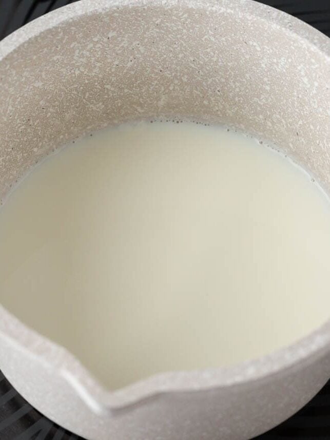 Milk warming in a saucepan on the stovetop for homemade Texas Roadhouse rolls.