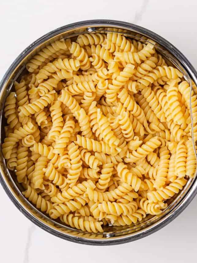 Cooked rotini pasta draining in a metal colander after rinsing.