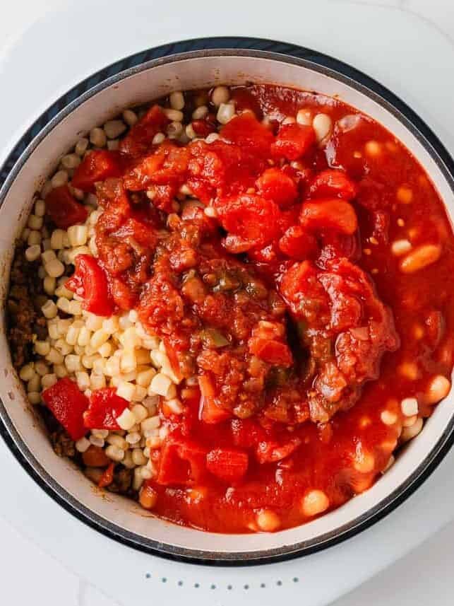 Beans, corn, diced tomatoes, salsa and tomato sauce added to seasoned ground beef in a Dutch oven.