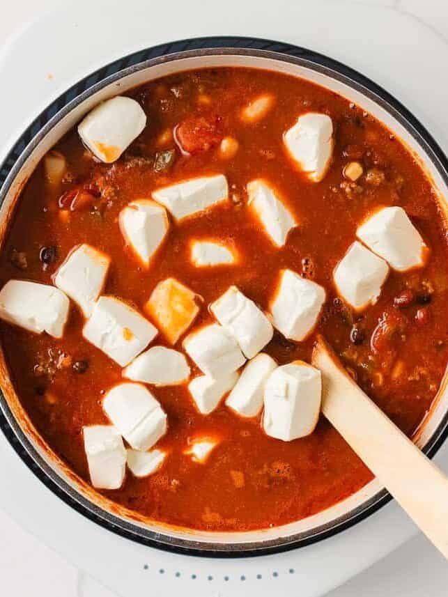 Cubes of cream cheese added to taco soup in a Dutch oven before stirring until smooth.