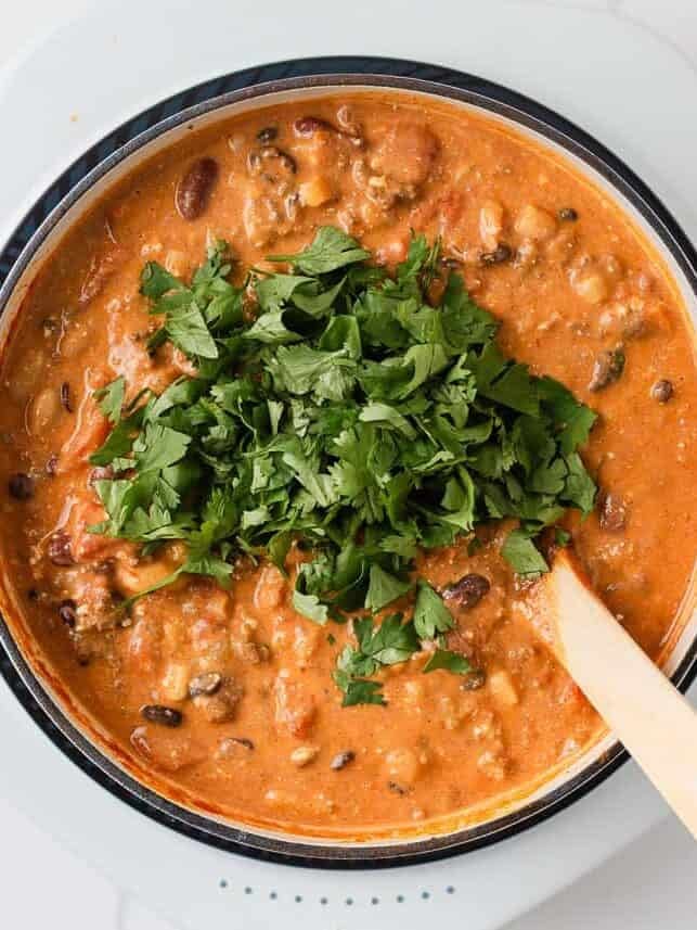 Finished creamy taco soup topped with chopped cilantro and stirred with a wooden spoon.