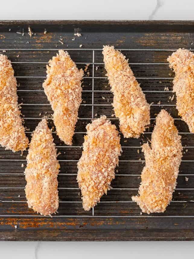 Breaded chicken tenderloins arranged on a wire rack before baking.
