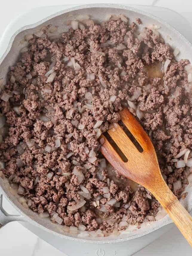 Browned ground beef and onions in a skillet for crockpot cowboy casserole.