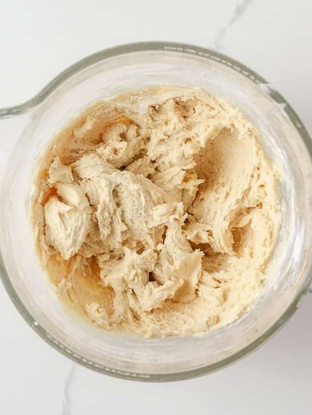 Thick sugar cookie dough mixed in a glass stand mixer bowl.
