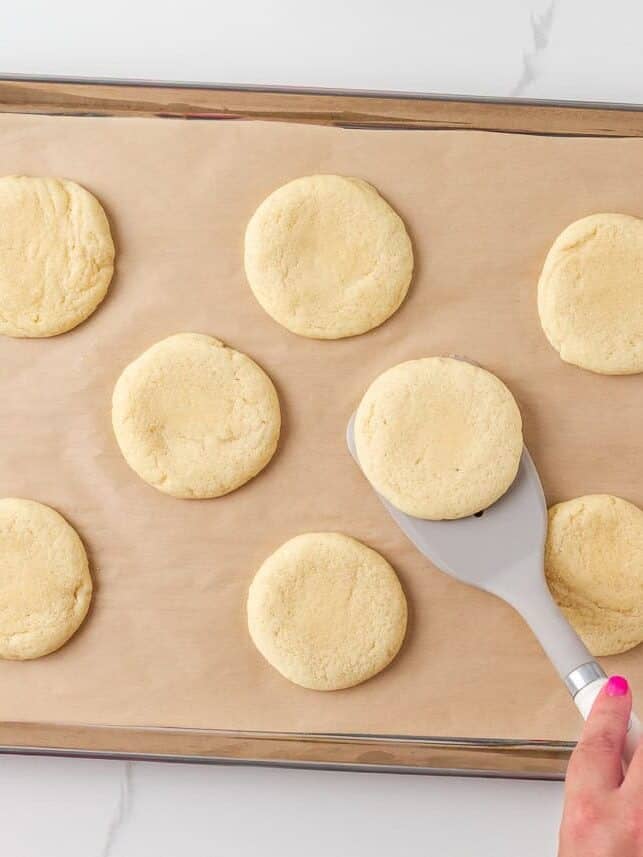 Freshly baked crumbl sugar cookies cooling on a parchment-lined baking sheet.