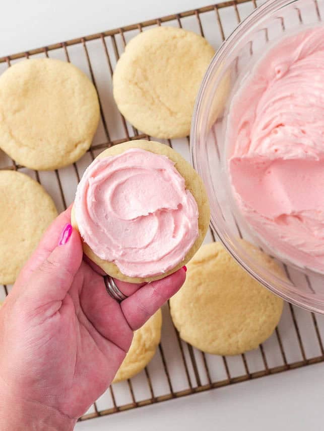 Frosting a cooled Crumbl sugar cookie with signature pink buttercream.