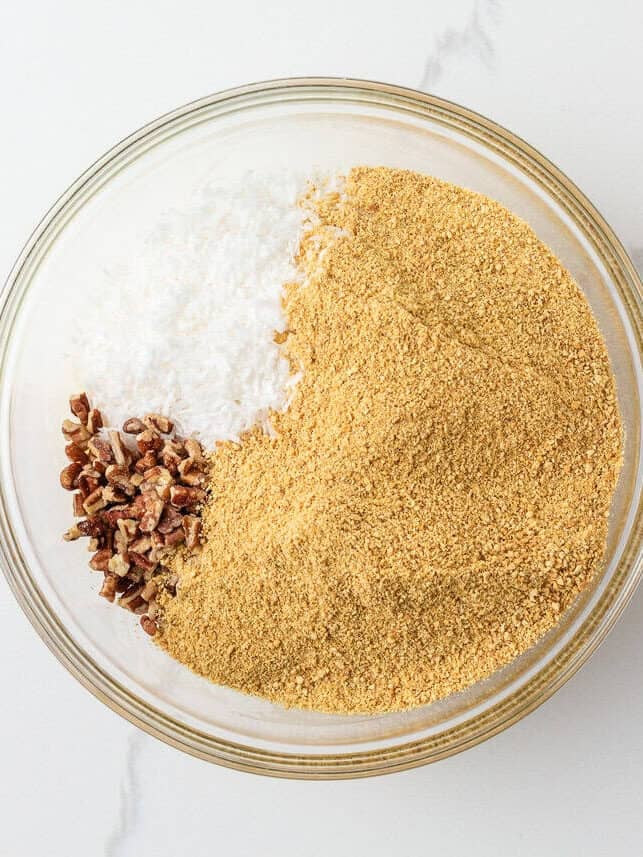 Graham cracker crumbs, shredded coconut and chopped pecans combined in a glass mixing bowl for 5 star bars.