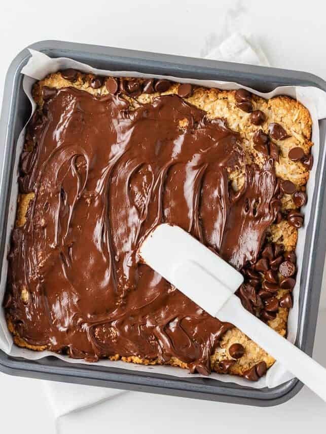 Melted chocolate chips being spread over baked 5 star bars with a spatula.