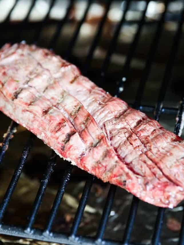 Marinated flank steak cooking on a hot outdoor grill.