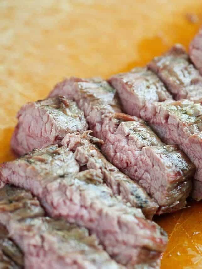 Juicy grilled flank steak sliced against the grain on a wooden cutting board.
