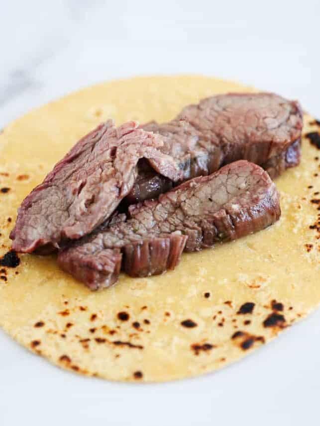 Sliced grilled flank steak arranged on a warm charred corn tortilla.
