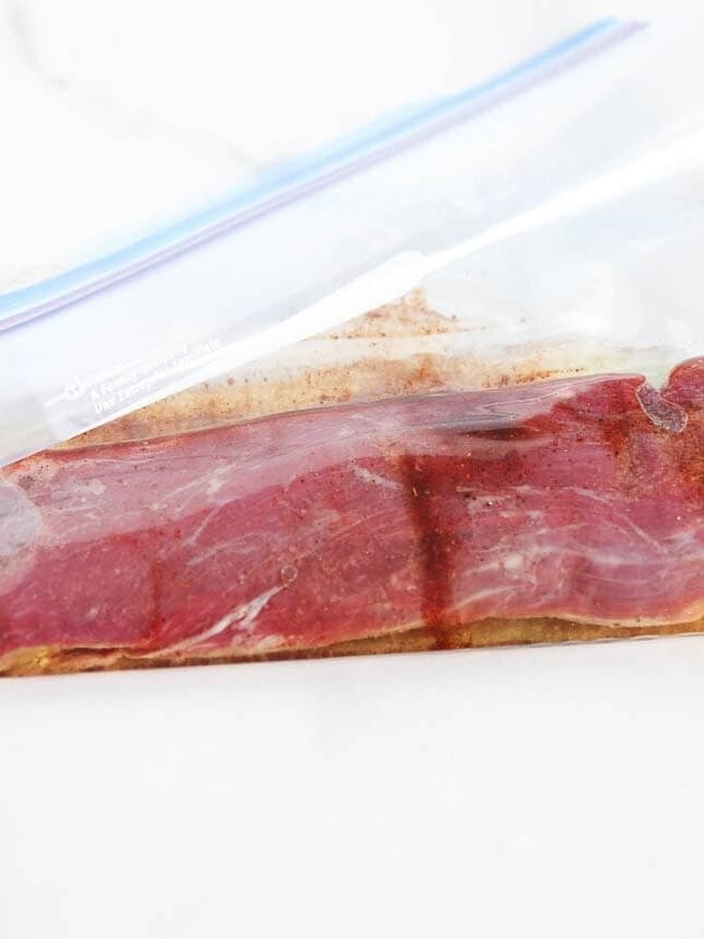Flank steak marinating with lime, garlic and spices in a zip-top bag.
