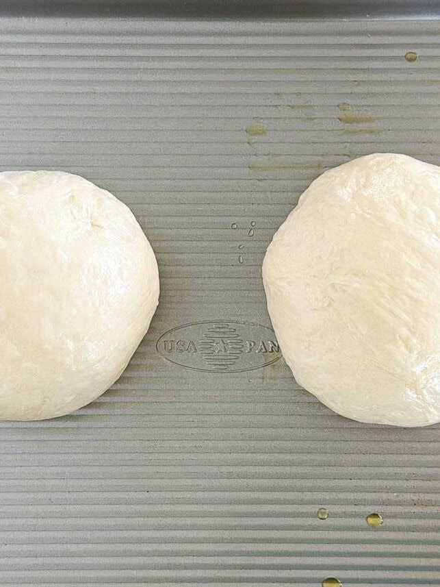 Two pizza dough balls on a pan.