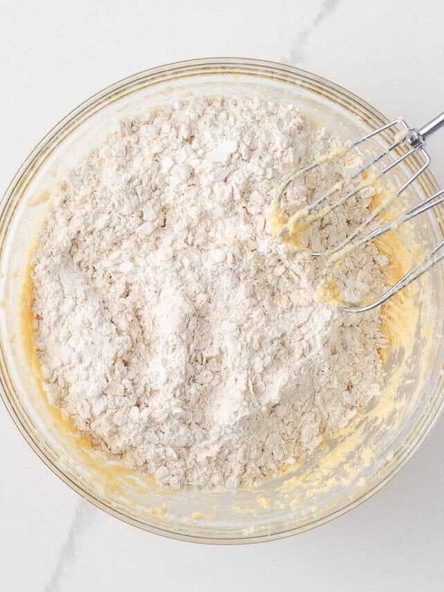 Dry ingredients being mixed into oatmeal cookie bar dough with a hand mixer.