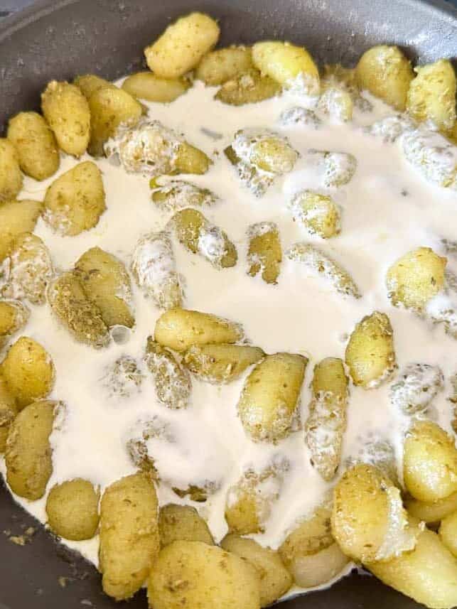 Pesto gnocchi being tossed with cream.