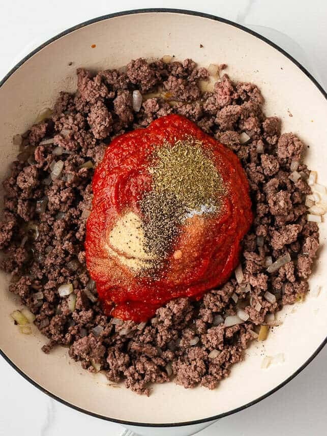 Ground beef and onions in a skillet with pizza sauce and seasonings added for making pizza burger filling.