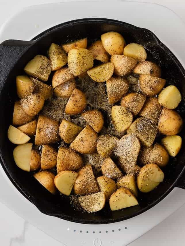 Baby gold potatoes cooking in butter and seasonings in a cast iron skillet.