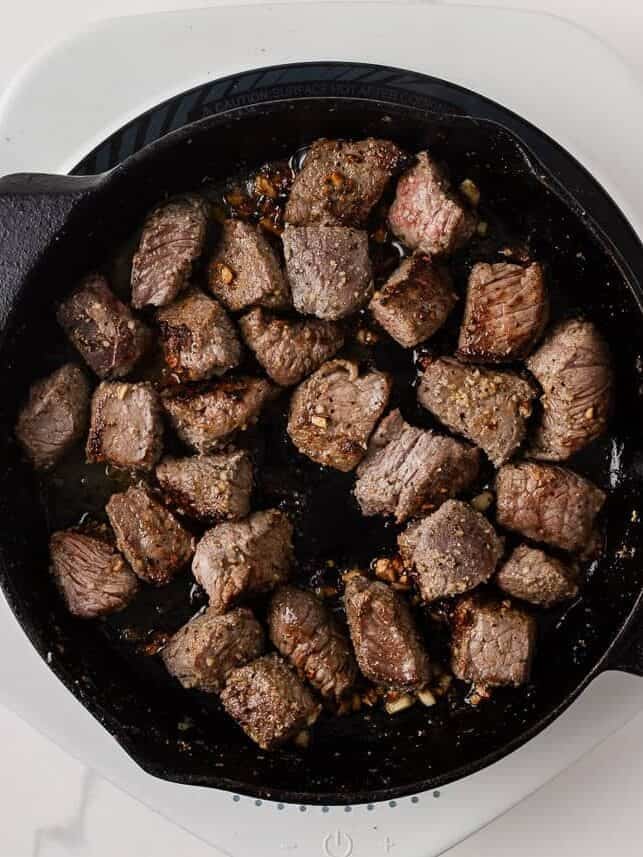 Seared sirloin steak bites cooking with garlic and butter in a cast iron skillet.