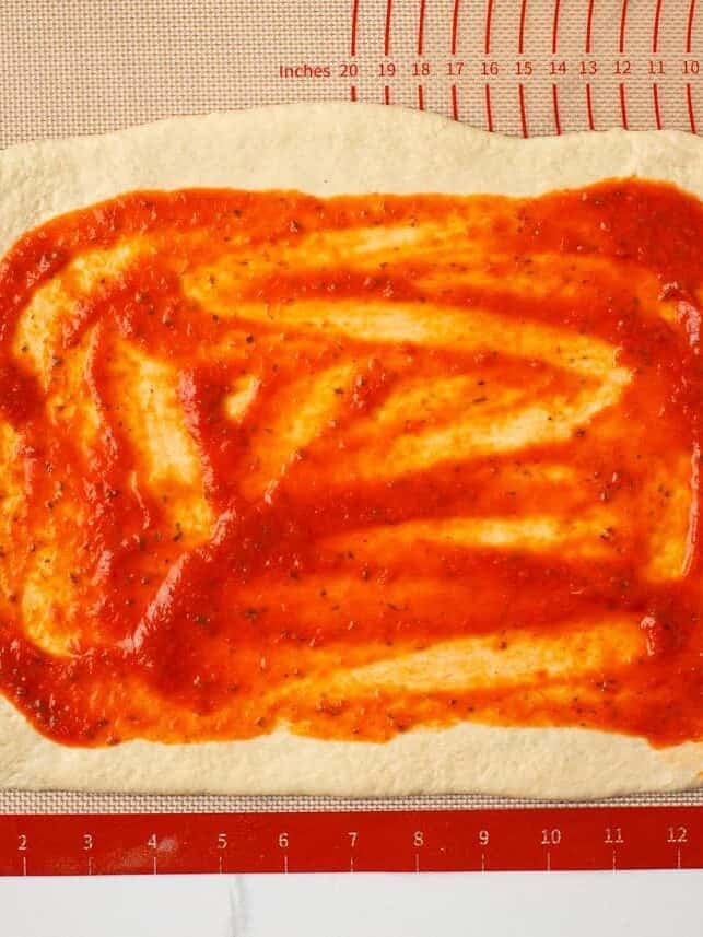 Pizza dough spread with pizza sauce for homemade stromboli.