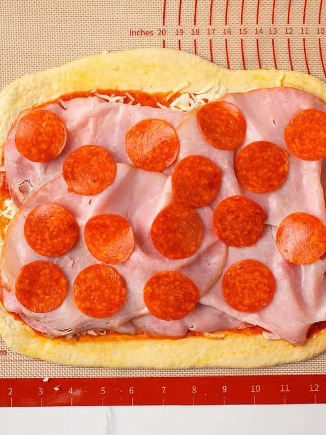 Pizza dough layered with ham, pepperoni, mozzarella and sauce before rolling into stromboli.