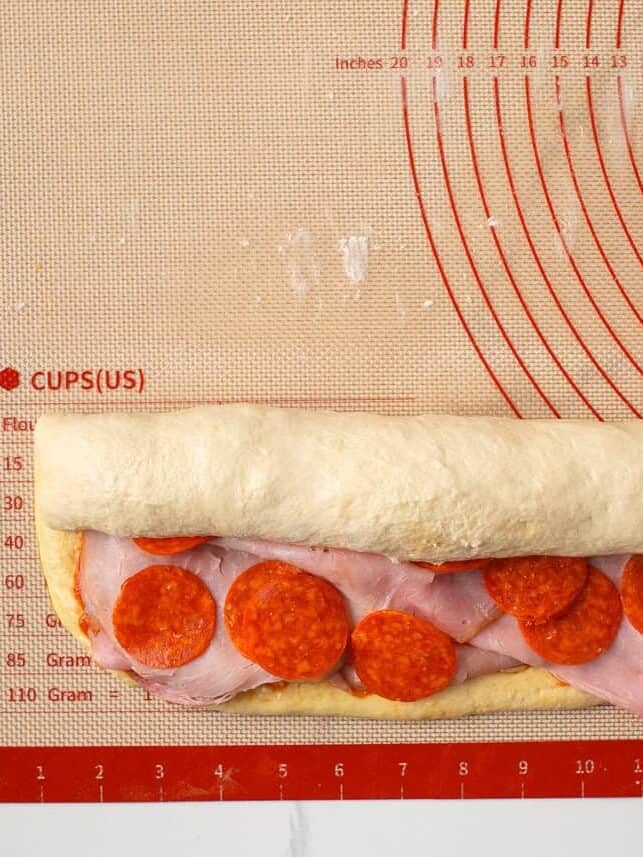 Stromboli dough being rolled around ham, pepperoni, cheese and pizza sauce.