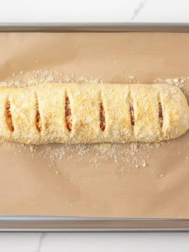Unbaked stromboli on a parchment-lined baking sheet with slits cut across the top.