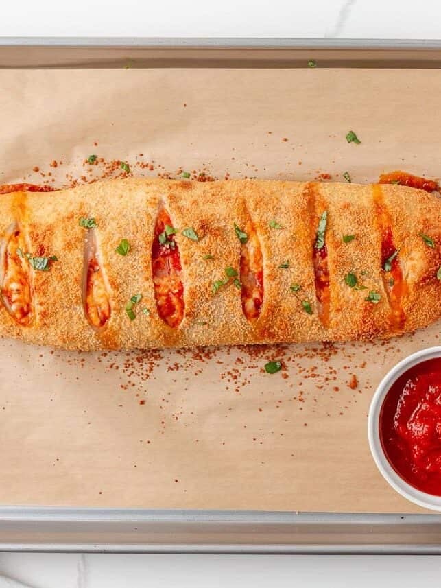 Freshly baked homemade stromboli on a baking sheet served with pizza sauce.
