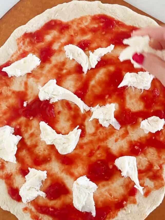 Adding fresh torn mozzarella to top of the pizza dough for a margherita pizza.