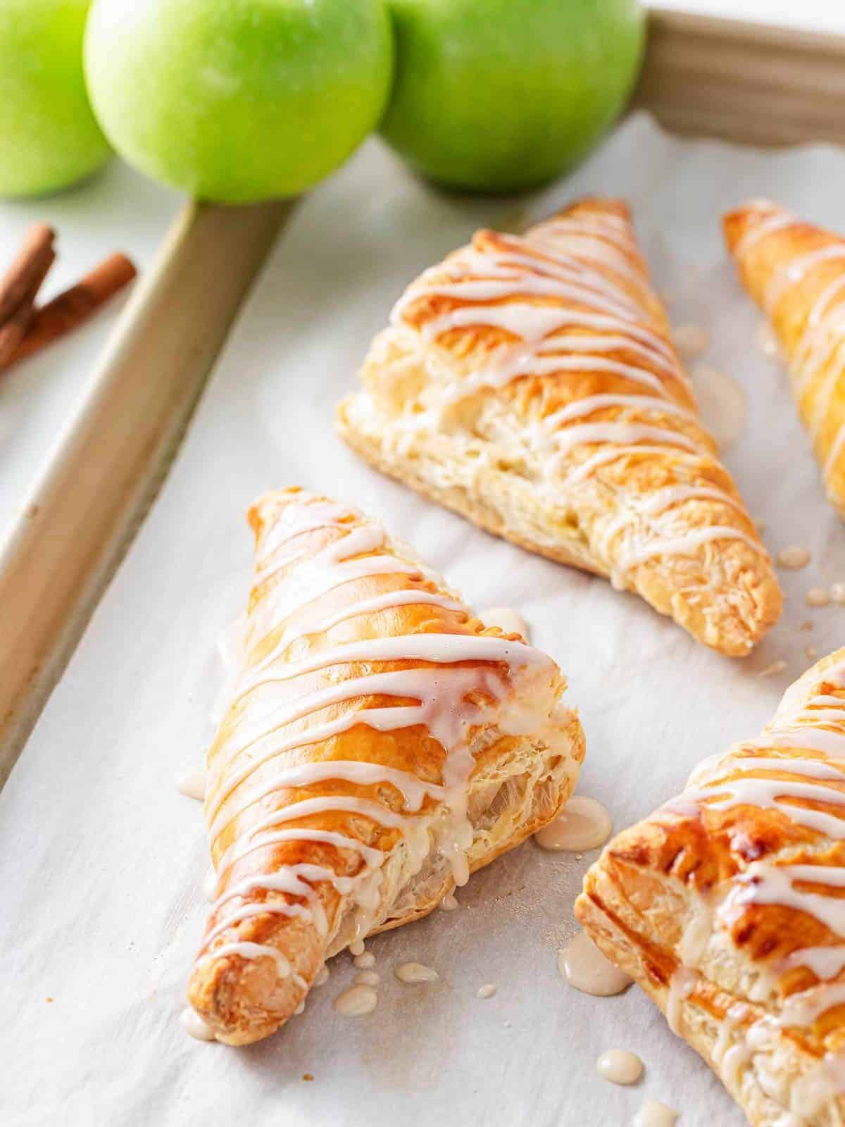 Apple turnovers on a baking sheet drizzled with icing.