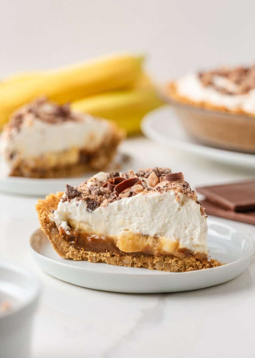 Slice of banoffee pie with banana and dulce de leche layers, whipped cream and chocolate toffee topping.