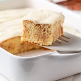 Slice of cinnamon roll poke cake lifted from the baking dish with a spatula.