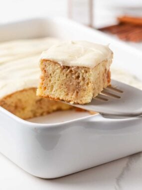 Slice of cinnamon roll poke cake lifted from the baking dish with a spatula.