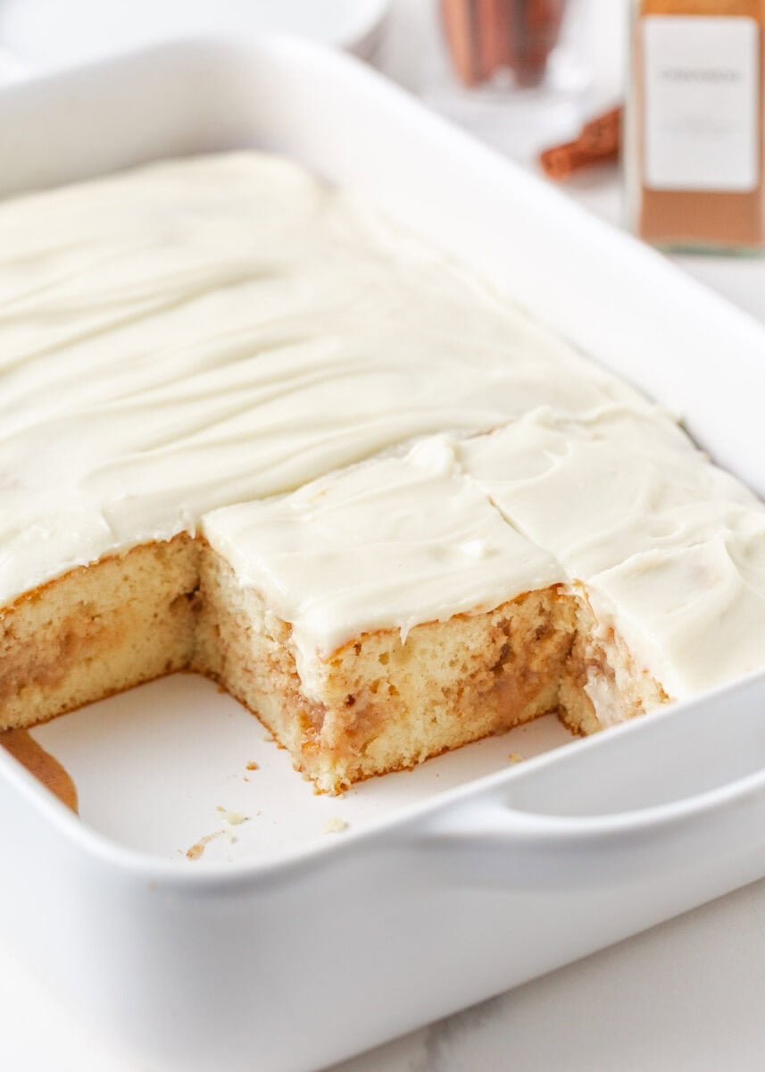 Frosted cinnamon roll poke cake with a few squares removed from the pan.