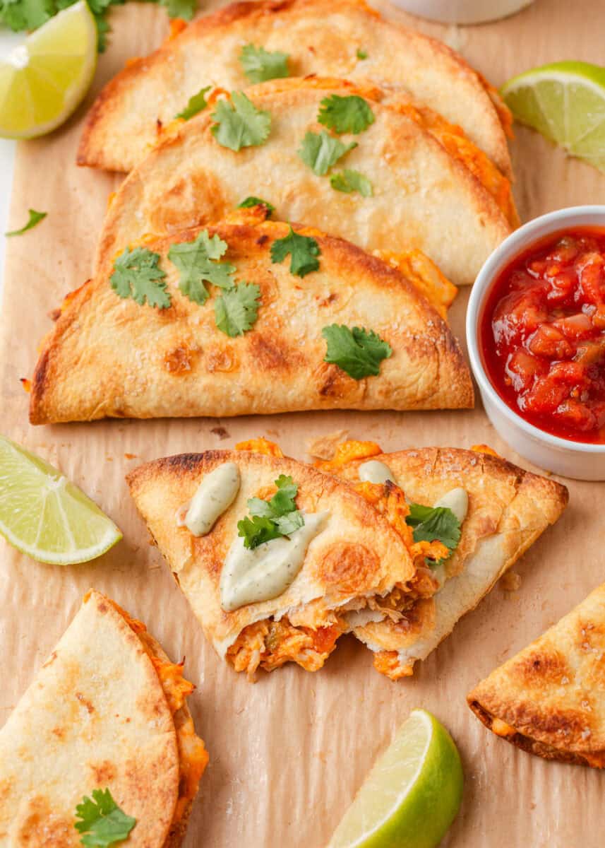 Crispy chicken tacos garnished with cilantro and served with salsa, creamy sauce and lime wedges.